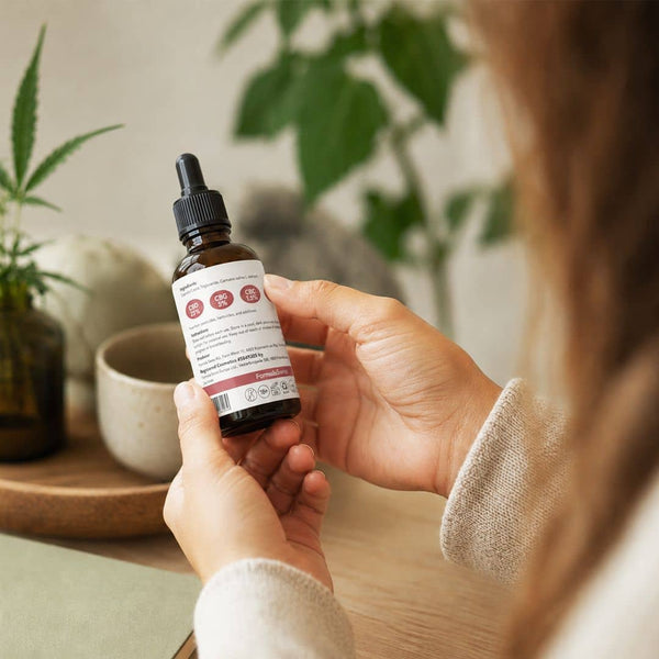 Femme examinant l'étiquette sur une bouteille d'huile de cannabinoïde Formula Swiss dans un cadre intérieur lumineux.